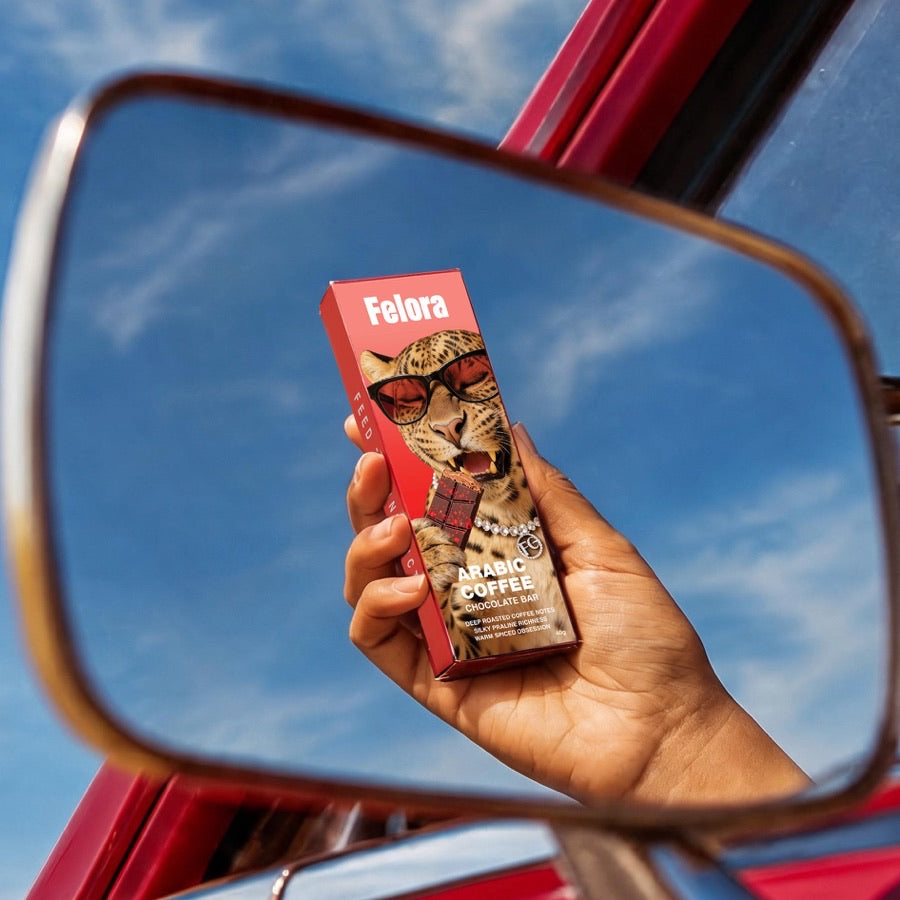 Felora Arabic Coffee chocolate bar held up in a car mirror against a blue sky